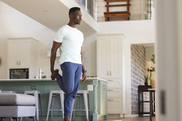Focused african american man practicing yoga standing holding foot at home, copy space