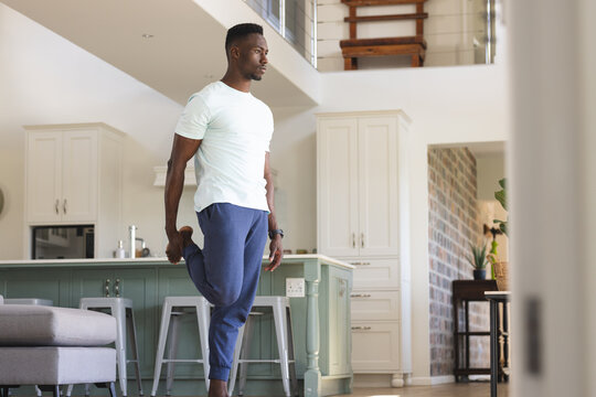 Focused african american man practicing yoga standing holding foot at home, copy space - Powered by Adobe
