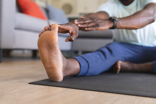 Low section of african american man practicing yoga, sitting and touching toes at home, copy space