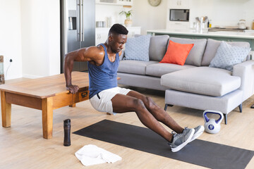 Fit african american man working out at home, doing push ups using coffee table