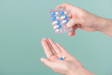 Medical pills. woman hands removing pills from panel on green background.