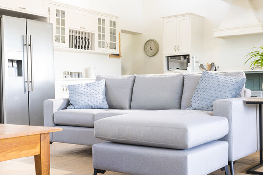 Grey l shaped sofa in sunny open plan living room with kitchen behind, copy space