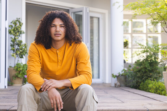 Young biracial man sits relaxed on a home porch
