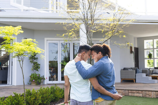Diverse gay couple embraces lovingly outdoors, with copy space