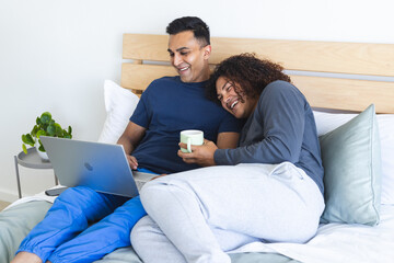 Gay biracial couple enjoys leisure time in bed, with copy space