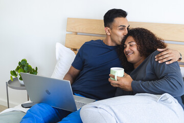 Middle Eastern man kisses a young biracial woman in a cozy bedroom setting