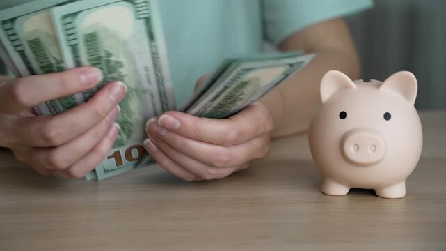 Person carefully counts a stack of paper money next to an adorable ceramic piggy bank, emphasizing a money-saving strategy for wealth accumulation.