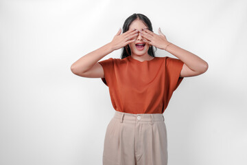 Young Asian woman in a brown shirt covering her eyes feeling scared isolated by white background. Concept of surprise or shock.