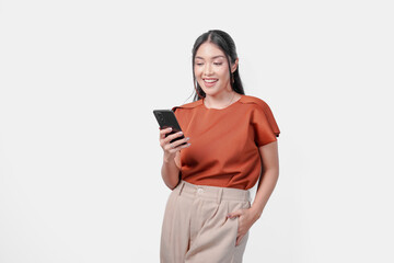 Naklejka premium Smiling young Asian woman in a brown shirt is using her smartphone to look at social media, isolated by white background.