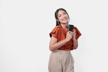 Happy mindful thankful young Asian woman smiling while holding phone with hands on chest over isolated white background.