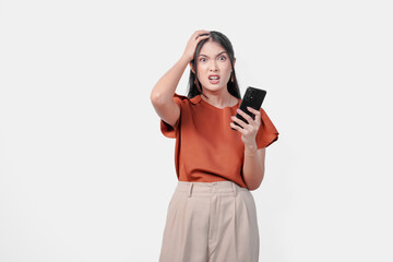 Naklejka premium Upset young Asian woman holding smartphone and appears to be angry over isolated white background.