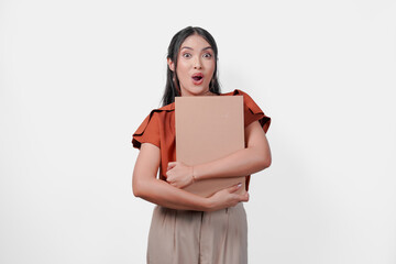 Curious young Asian woman is hugging a gift box with surprised expression.