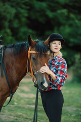 Obraz premium Happy blonde with horse in forest. Woman and a horse walking through the field during the day. Dressed in a plaid shirt and black leggings.