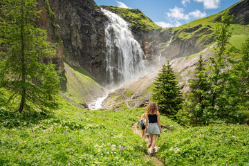 backview of female hikers at  Engstligen waterfall during summer. Wild flowers in foreground. Wonderful hiking spot, majestic cascade in Swiss Alps, Switzerland beautiful nature. Must-see hiking spot.