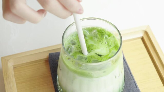 Glass of iced matcha green tea latte being stirred with a straw