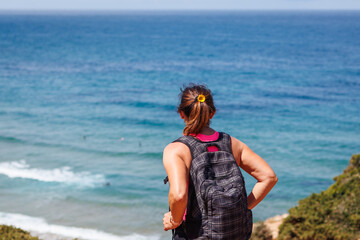 Sporty mature woman enjoying view from cliff to sea during hike on trekking trail along Algarve coast in Portugal. Active summer vacation