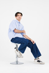 Portrait of asian male confidence charming handsome young guy, Wearing blue collar shirt and jeans posing relaxed looking attractive sitting on chair in white background studio - isolated