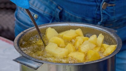 Potatoes in boiling oil. Close-up of potatoes frying in hot oil. Potato pieces surrounded by bubbles from boiling oil during cooking. French fries. Selective focus.