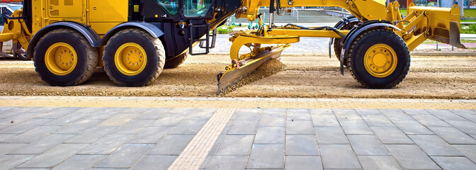 The grader levels the road. The blade of a motor grader in the process of leveling the sandy base...