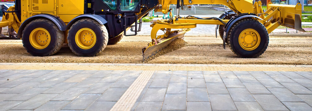 The grader levels the road. The blade of a motor grader in the process of leveling the sandy base of the road. A grader works on road construction.