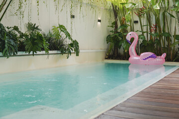 A pink inflatable flamingo floats in a pool. The pool is in a backyard, and there are two lounge chairs on the deck.
