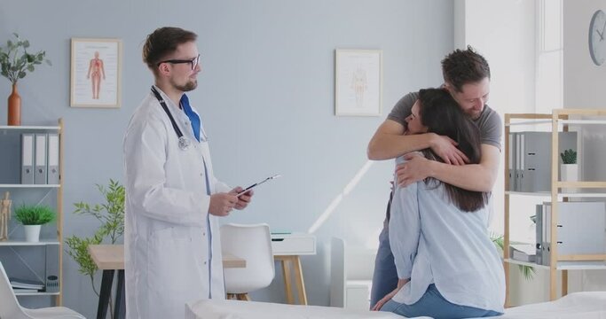 Doctor telling good news about recovery, test result to woman patient and husband in clinic. Congratulating on positive condition, pregnancy announcement, happy reproductive treatment. Doctor couple.