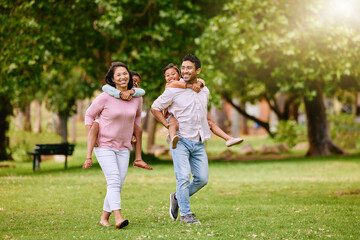 Fototapeta premium Family, park and walking with piggy back for wellness or happiness, together in nature for bonding. Mixed race people, children and parents on grass for vacation in Europe, smile for travel with kids