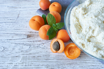 A bowl of cottage cheese with apricots and mint on a wooden background. Cooking the cake.