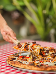 Woman hand takes a slice of pizza with spatula on table.