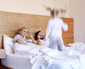 Parents, bed and tired from jumping child, adhd and chaos in home bedroom on weekend. Excited, energy and girl with motion blur for speed, headache and stress or overwhelmed man and female person
