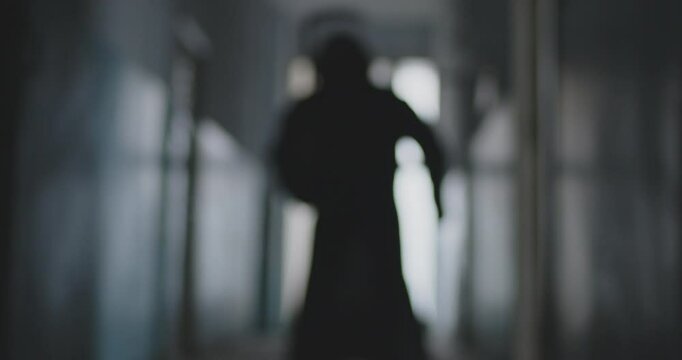Halloween day. Silhouette of a reaper with a death scythe wandering along the corridor in the dark. Horror and fear atmosphere. Abstract video of a dark hallway, with blurred silhouette.