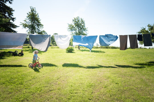 A child riding a bike under a laundry line sheets hanging to dry