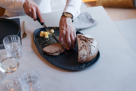 Person slicing fresh bread on a black plate with butter curls
