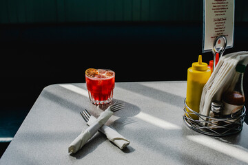 Red cocktail on a diner table with condiments and napkins.
