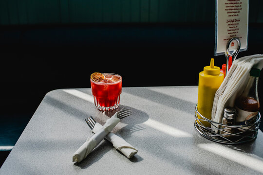 Red cocktail on a diner table with condiments and napkins.