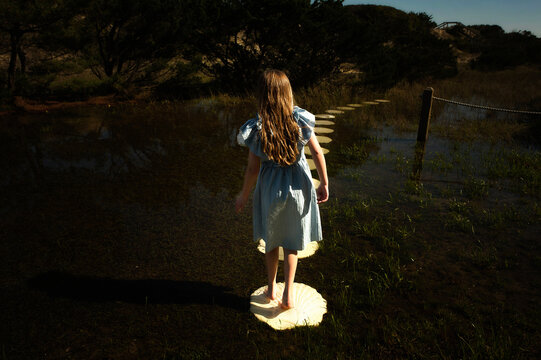 Young girl walking stone path through flooded field