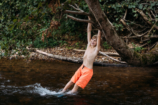 Smiling child swinging on tree branch over river during summer
