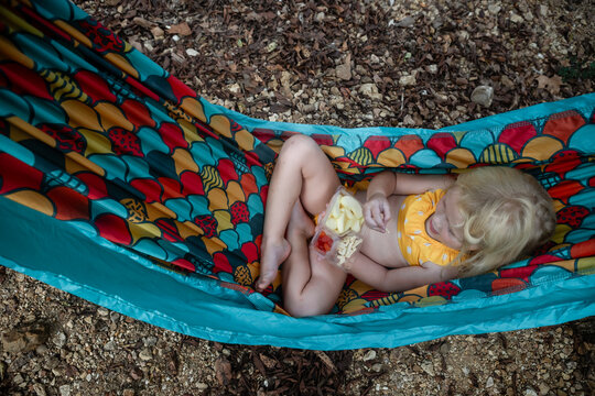 Young child eating snack in hammock during summer time