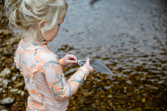 Young girl holding found bird feather at river