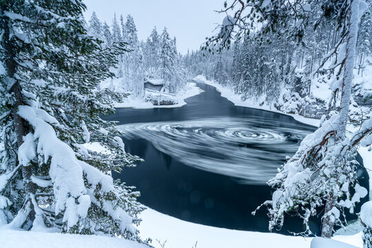 Frozen rapids vortex in a snowy forest near Myllykoski mill, Finland