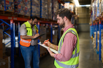 Warehouse worker in safety uniform check the stock order details and goods supplies in the...