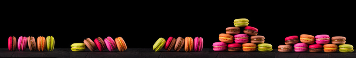 French colorful macaroons in row on wooden table isolated on black