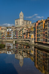 Obraz premium A view of the colourful buildings and Cathedral of Saint Mary of Girona reflected in the River Onya