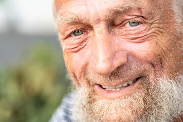 close-up portrait of happy senior man looking at camera. Park in background, Elderly mature people in outdoors leisure activity alone. One old male with beard and blue eyes look at you. Happiness