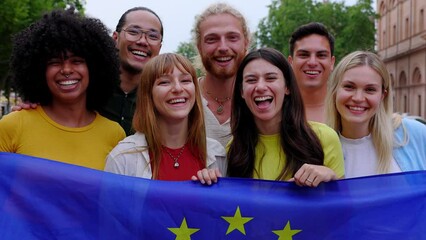 Diverse group of people holding European Union Flag while smiling at the camera standing together outdoors