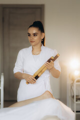 Masseuse massaging leg of client and foot of girl. Manual, aesthetic procedures in spa salon. Lymphatic drainage for increased blood and lymph flow. Gua Sha, gouache scraper device, bamboo sticks.