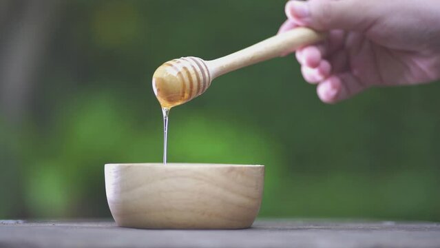 Honey dripping, pouring from honey dipper in a wooden bowl. Slow-motion
 - Powered by Adobe