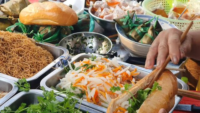 Woman making vegan Vietnamese bread or banh mi, popular Vietnam street food, raw material in tray, hands stuffing ingredient into sandwich to make delicious meal
