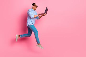 Full length photo of handsome confident guy wear plaid shirt jumping communicating modern gadget emtpy space isolated pink color background