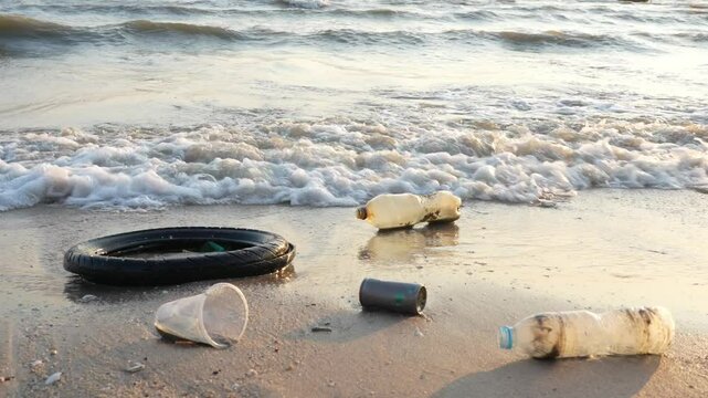 Environmental pollution earth day concept. Trash on the beach left by tourist with ocean waves and evening light at sunset. Bangsaen Sea coast of Thailand.